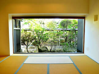 This serene room features tatami mats and a large window showcasing a meticulously landscaped Japanese garden.