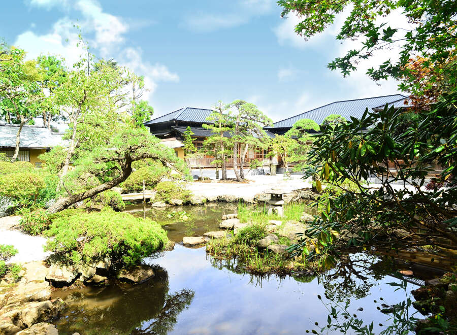 Discover serenity in this Japanese garden, featuring a tranquil pond reflecting the surrounding lush greenery and traditional architecture.
