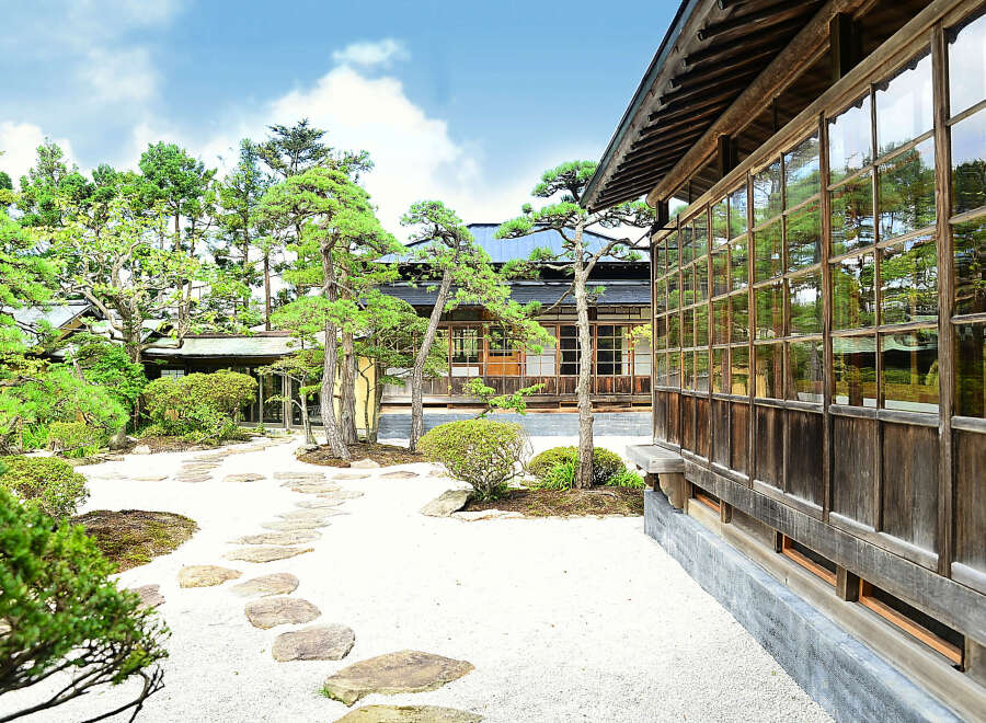 This serene Japanese garden features a traditional wooden house with expansive windows, offering stunning views of the meticulously landscaped grounds.