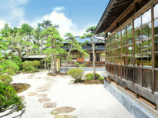 This serene Japanese garden features a traditional wooden house with expansive windows, offering stunning views of the meticulously landscaped grounds.