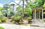 This serene Japanese garden features a traditional house with large windows, surrounded by meticulously manicured trees and shrubs.