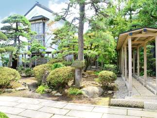This serene Japanese garden features a traditional house with large windows, surrounded by meticulously manicured trees and shrubs.
