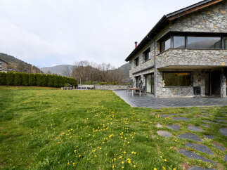 This stunning stone house boasts a spacious backyard perfect for outdoor entertaining, complete with a patio and a lush lawn dotted with dandelions.