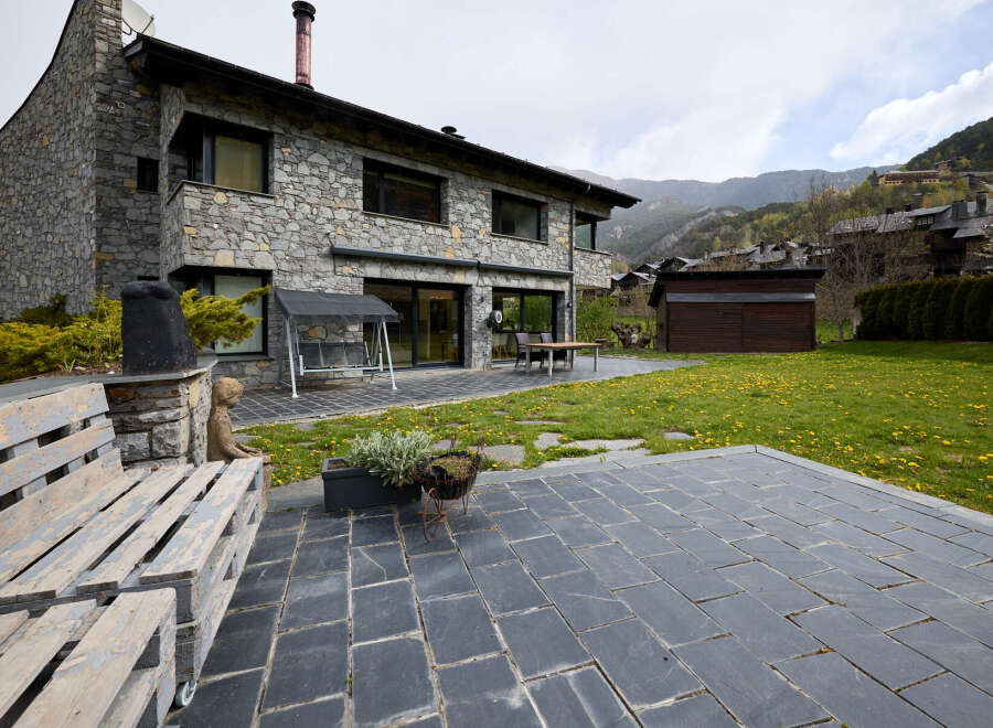 This stunning stone house boasts a spacious patio perfect for outdoor entertaining, complete with a charming pallet bench and a tranquil garden view.