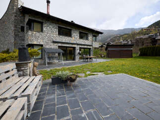 This stunning stone house boasts a spacious patio perfect for outdoor entertaining, complete with a charming pallet bench and a tranquil garden view.