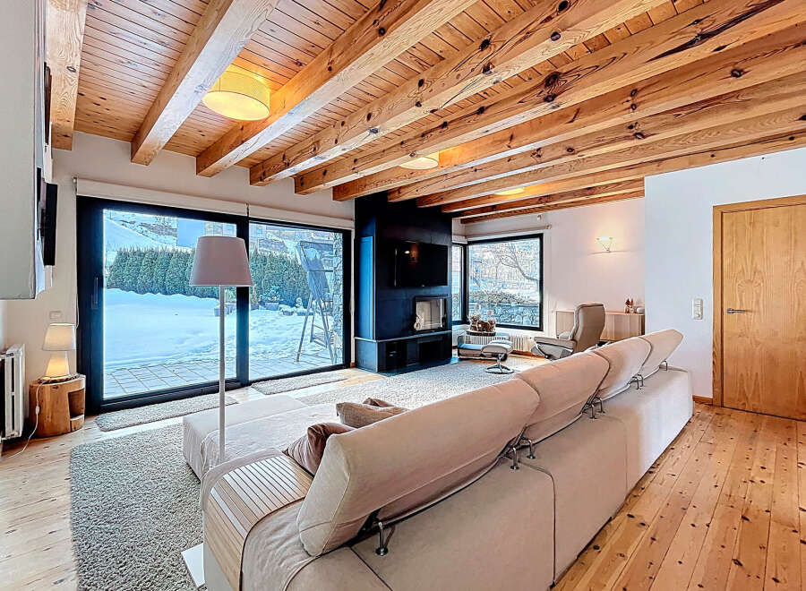 This stunning living room boasts a cozy ambiance with its wooden ceiling and flooring, complemented by a modern fireplace and large windows that offer scenic views.