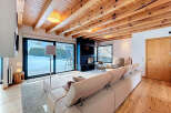 This stunning living room boasts a cozy ambiance with its wooden ceiling and flooring, complemented by a modern fireplace and large windows that offer scenic views.