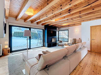 This stunning living room boasts a cozy ambiance with its wooden ceiling and flooring, complemented by a modern fireplace and large windows that offer scenic views.