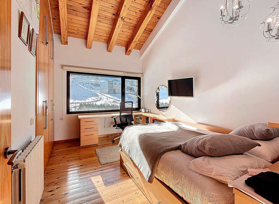 This stunning bedroom boasts a unique design with a wooden ceiling and a large window offering breathtaking views of a snowy landscape.