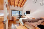 This stunning bedroom boasts a unique design with a wooden ceiling and a large window offering breathtaking views of a snowy landscape.