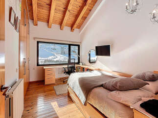 This stunning bedroom boasts a unique design with a wooden ceiling and a large window offering breathtaking views of a snowy landscape.
