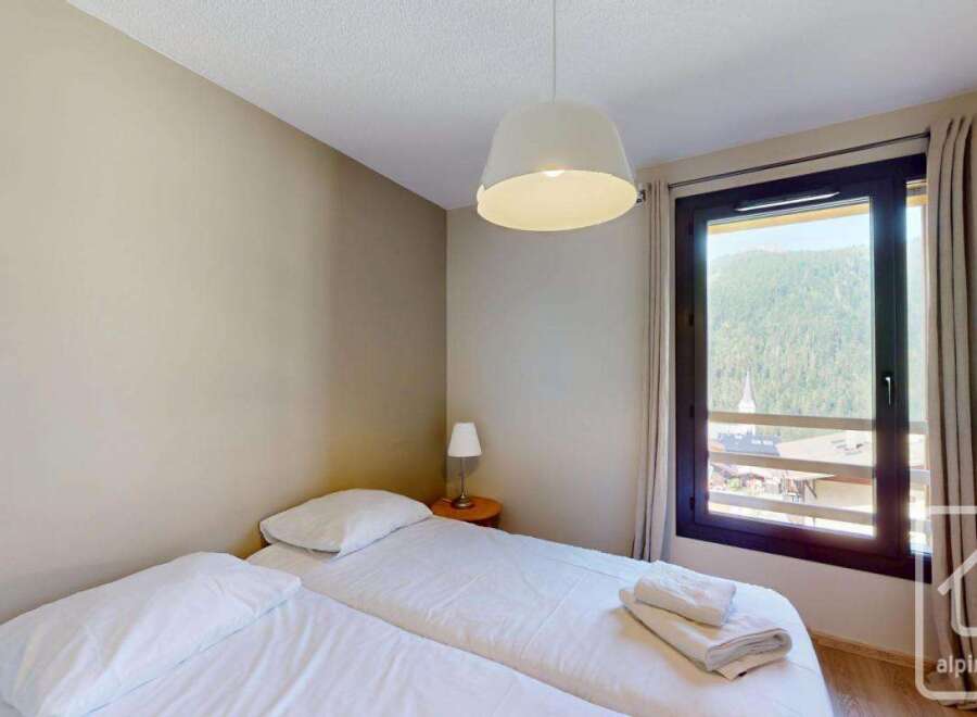 This cozy bedroom features a comfortable double bed, offering stunning mountain views through a large window.