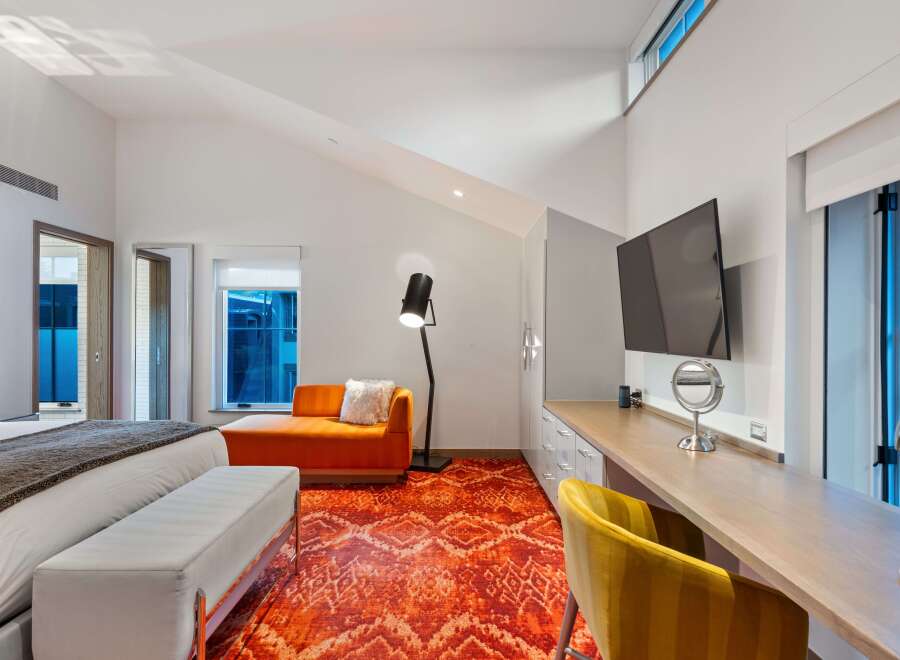 Experience luxury in this stunning bedroom featuring a vibrant orange rug and a stylish chaise lounge.