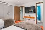 Discover a stylish bedroom featuring a modern design with a sleek TV and a chic wooden console.