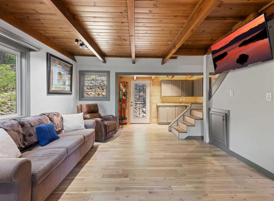 This stunning cabin boasts a spacious living area with hardwood floors, a cozy sofa, and a wood-beamed ceiling.