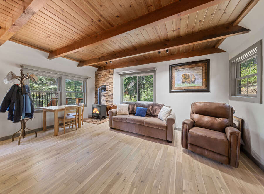 Cozy cabin living room with wood-beamed ceiling, wood flooring, and a stone fireplace.