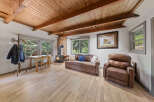 Cozy cabin living room with wood-beamed ceiling, wood flooring, and a stone fireplace.