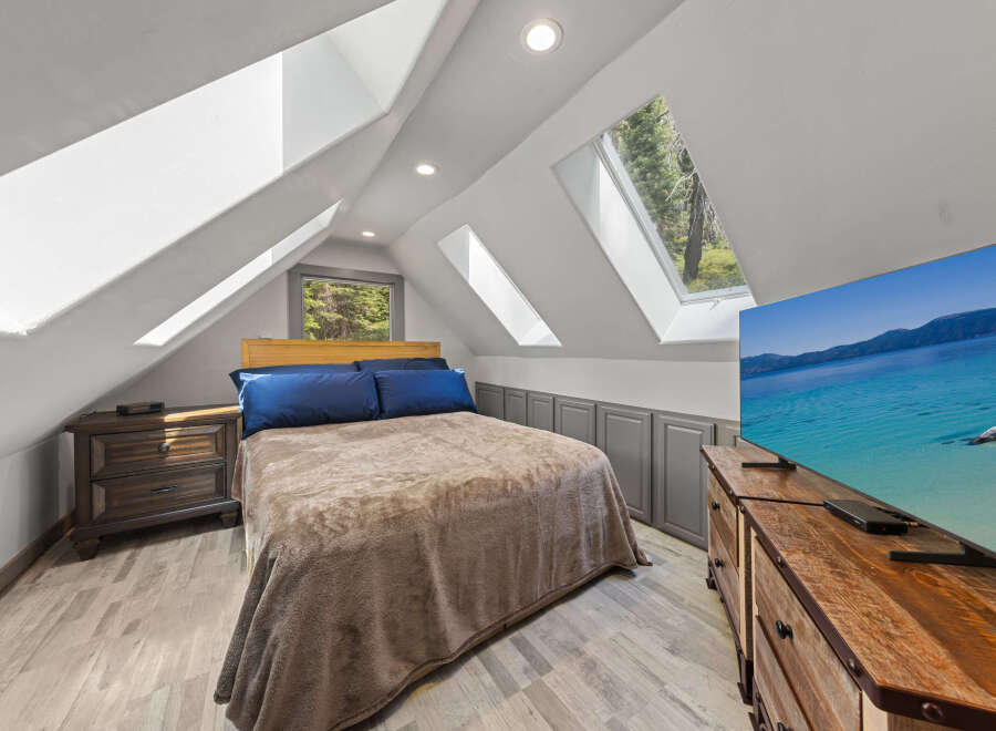 Cozy attic bedroom with a queen-size bed, large TV, and plenty of natural light from skylights.