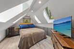 Cozy attic bedroom with a queen-size bed, large TV, and plenty of natural light from skylights.