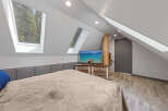 Cozy attic bedroom with plush bedding, rustic wood dresser, and a flat-screen TV showcasing a scenic lake view.