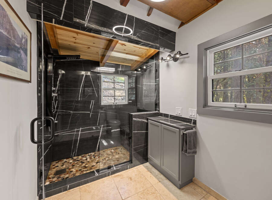 This stunning bathroom boasts a walk-in shower with pebble flooring and sleek black marble tile.