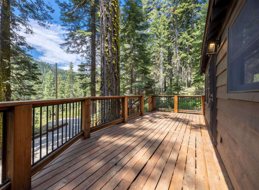 This stunning cabin boasts a spacious deck with a wooden floor and metal railing, offering breathtaking views of the surrounding forest.