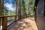 This stunning cabin boasts a spacious deck with a wooden floor and metal railing, offering breathtaking views of the surrounding forest.