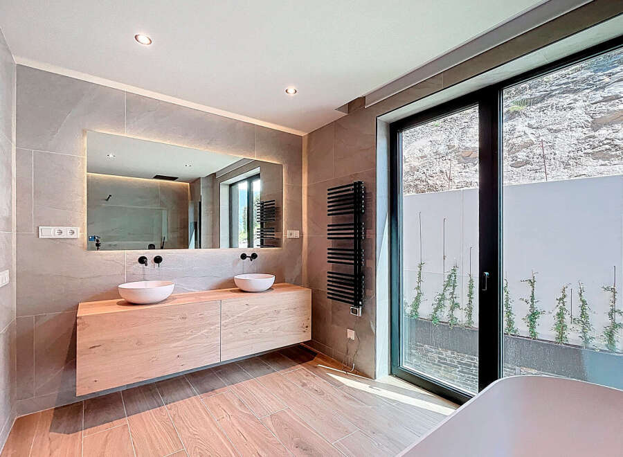 This modern bathroom boasts a sleek design with a floating wooden vanity and two stylish vessel sinks.