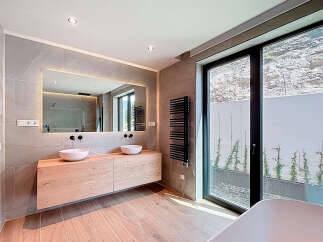 This modern bathroom boasts a sleek design with a floating wooden vanity and two stylish vessel sinks.