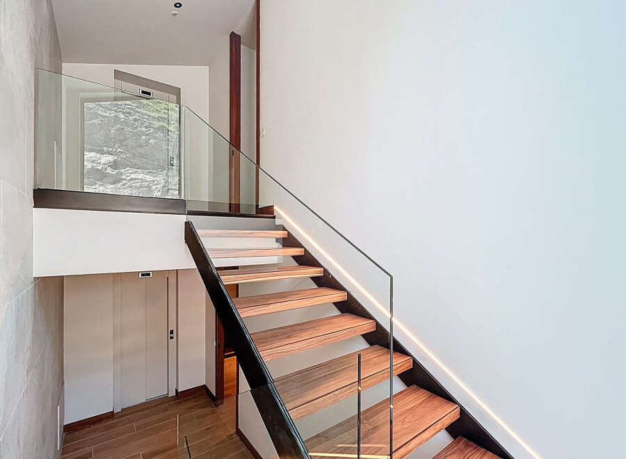 Discover the elegance of this modern staircase, featuring sleek glass railings and warm wooden steps.