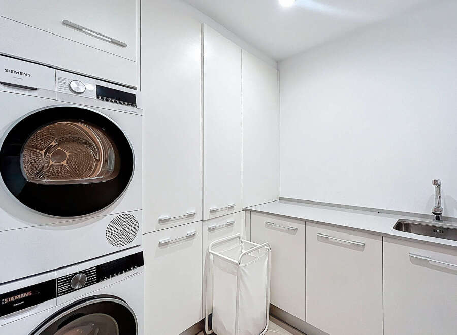 This modern laundry room features sleek white cabinetry and a convenient sink area.