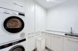 This modern laundry room features sleek white cabinetry and a convenient sink area.