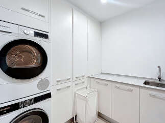 This modern laundry room features sleek white cabinetry and a convenient sink area.