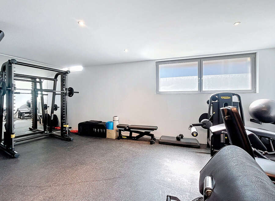 Step into your personal fitness sanctuary! This home gym boasts a comprehensive setup, including a Smith machine, weight bench, and various exercise equipment.