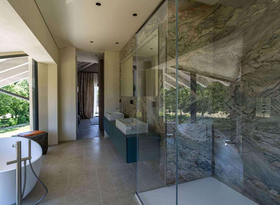 This luxurious bathroom boasts modern design elements, including a standalone bathtub with stylish fixtures and a glass-enclosed shower featuring stunning marble walls.