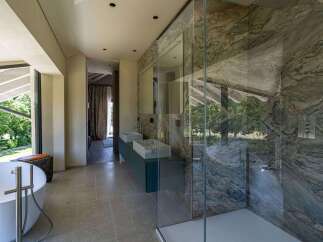 This luxurious bathroom boasts modern design elements, including a standalone bathtub with stylish fixtures and a glass-enclosed shower featuring stunning marble walls.