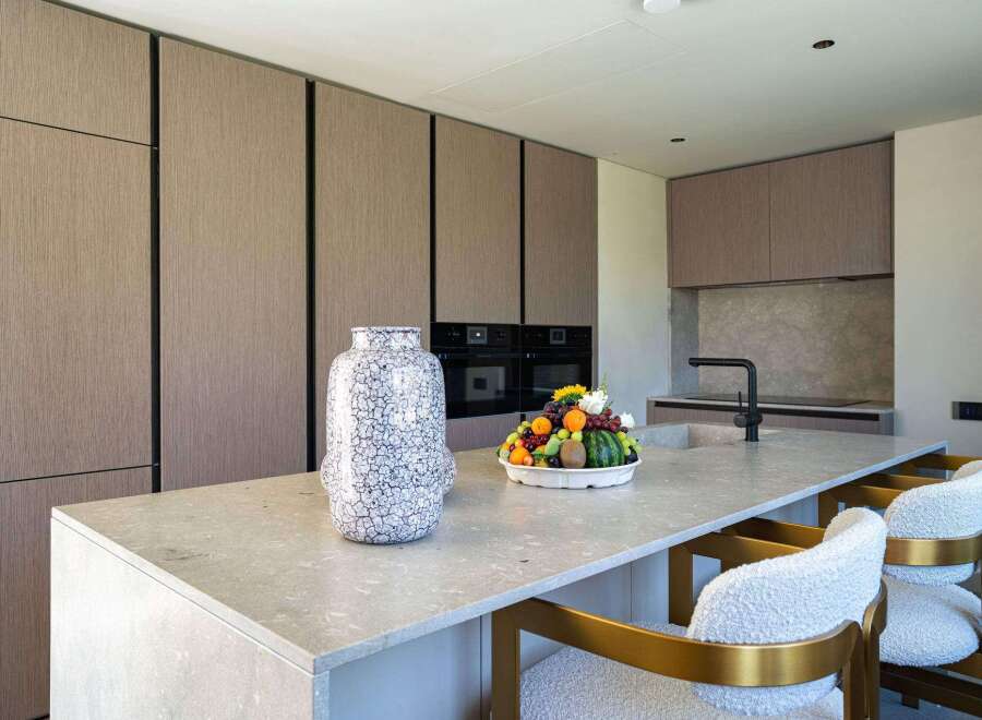 This modern kitchen boasts sleek, handleless cabinetry with a wood-grain finish, complemented by a spacious island topped with a light-colored stone countertop.