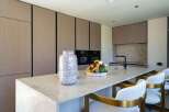This modern kitchen boasts sleek, handleless cabinetry with a wood-grain finish, complemented by a spacious island topped with a light-colored stone countertop.