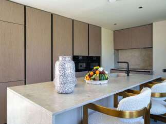 This modern kitchen boasts sleek, handleless cabinetry with a wood-grain finish, complemented by a spacious island topped with a light-colored stone countertop.