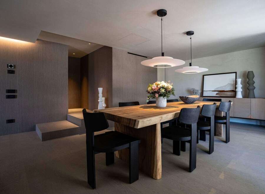 This dining room features a solid wood table paired with modern black chairs, illuminated by sleek pendant lights.