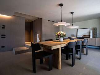 This dining room features a solid wood table paired with modern black chairs, illuminated by sleek pendant lights.