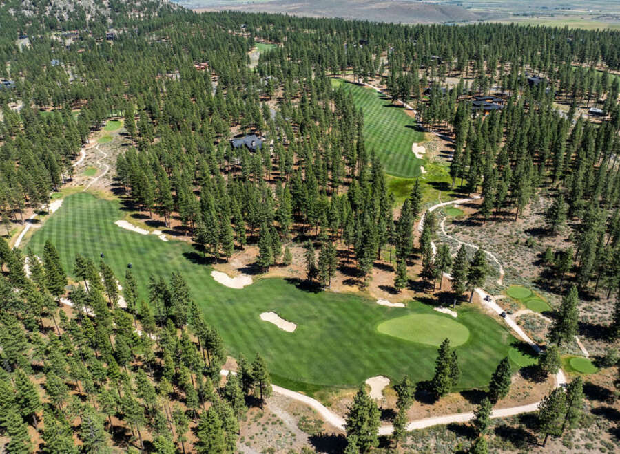 An aerial view showcases a golf course nestled within a dense forest.