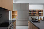 Modern kitchen with sleek gray and wood cabinetry, a built-in bookshelf, and a large island with a dark countertop and integrated sink.