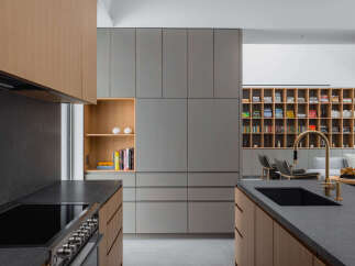 Modern kitchen with sleek gray and wood cabinetry, a built-in bookshelf, and a large island with a dark countertop and integrated sink.