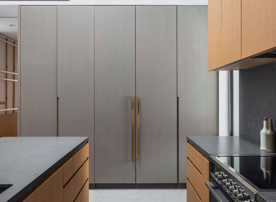 This stunning kitchen boasts sleek, gray cabinetry with brushed gold hardware, complemented by warm wood tones on the lower cabinets and countertops.
