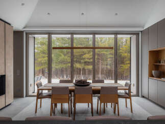 This stunning modern home boasts a spacious dining area with floor-to-ceiling windows offering breathtaking views of a snow-dusted forest.