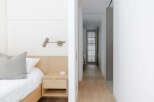 This modern bedroom features a minimalist design with a light wood nightstand and a white upholstered headboard.