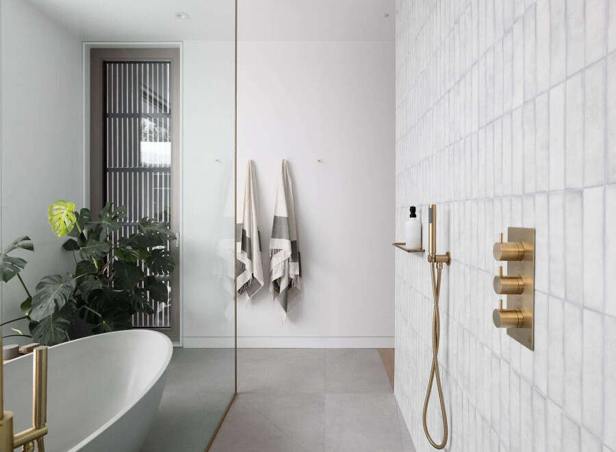 This stunning bathroom boasts a freestanding bathtub, a walk-in shower with brass fixtures, and a sleek glass partition.