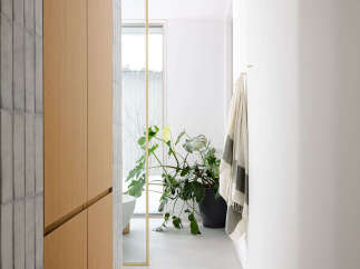 This modern bathroom boasts a sleek design with light grey tiles, light oak cabinetry, and a large, lush plant adding a touch of nature.