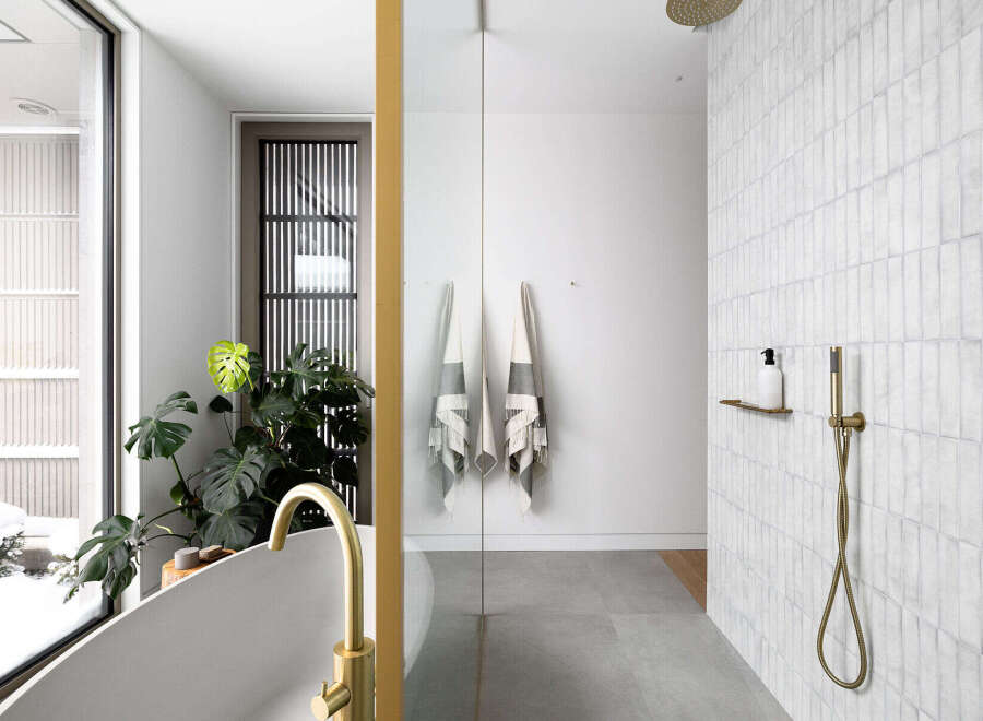 This luxurious bathroom boasts a spacious walk-in shower with sleek gold fixtures and subway tiles, complemented by a freestanding bathtub with a gold faucet.